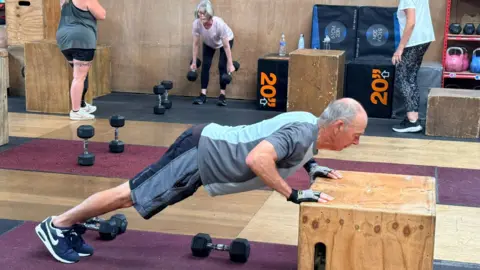 Krish Stevens A man wearing fitness clothing standing in a gym surrounded by weightlifting equipment