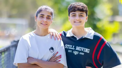 Jack Tran Atefeh Ramezanisadeh (L) and Fatemeh Pasandideh pose for a photo, blurred greenery in the background