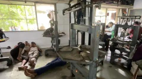 A decrepit diamond polishing unit shows ageing machinery and workers lying down on the floor, looking at their phones in Surat, India.