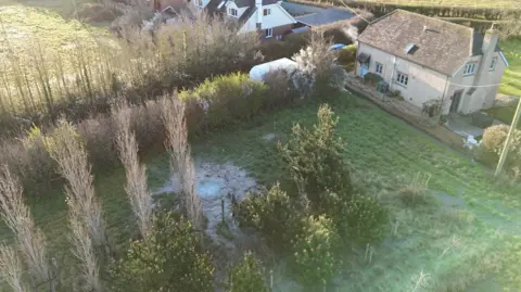 Large pool of water - looking like a pond in a field on the Isle of Wight to the back of several houses.