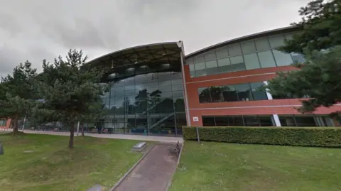 A large commercial building. There are three trees in front of it.