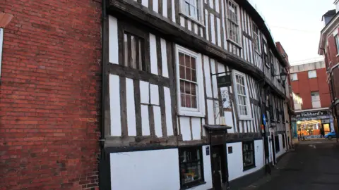Terence Lloyd A white timber framed two-storey building down a narrow road
