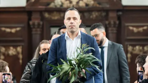 Jenny Magee Photographer Ray Ingrey leading a small procession of people walking up the aisle at the Wren Library, Trinity College, Cambridge