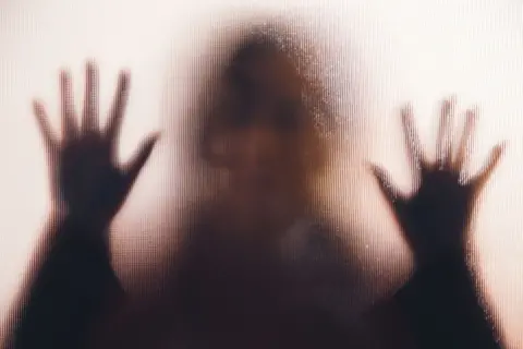 Getty Images A woman's silhouette, her hands against a frosted glass window