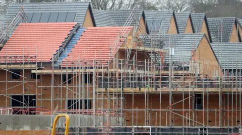A construction site with newly built houses situated behind some scaffolding.
