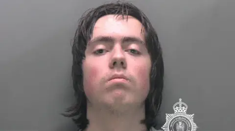 North Wales Police Image released by North Wales Police of 18-year-old Tristan Roberts. He has shoulder length black hair, is expressionless and looks straight at the camera.