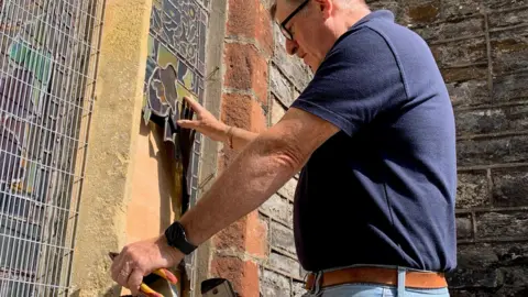 Diocese of Exeter The Reverend Andrew Johnson examines the damage to a stained-glass window.