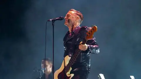 Getty Images Penyanyi Kanada Bryan Adams yang mengenakan jaket kulit hitam dan celana hitam memegang gitar di tangannya dan di depannya terdapat mic stand selama penampilannya di NESCO Centre, Goregaon pada 13 Desember 2024 di Mumbai, India.