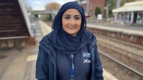 BBC Trainee train driver Amina Ibrar standing next to a railway line smiling