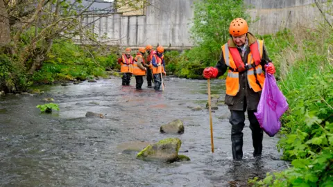 Yorkshire Wildlife Trust People wearing fluorescent safety helmets and jackets standing in a river 
