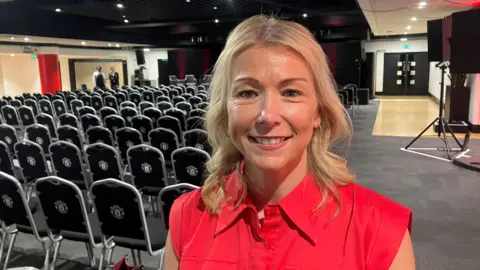 Photograph of Collette Roche from Manchester United. The image shows her in a function room, with chairs and a stage at Old Trafford.