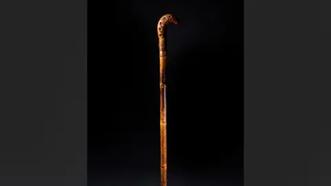 Norfolk Museums Service An ornate wooden walking stick against a black backdrop