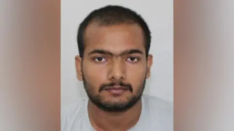 Northamptonshire Police Police photo of Pankaj Lamba, with short, dark hair and beard. He is wearing a gray t-shirt.