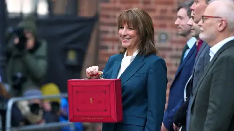 PA Media A woman in a blue suit holds a read despatch box