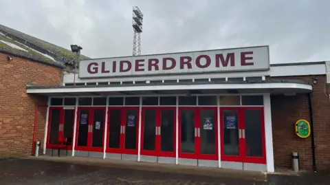 Karl Bird/BBC The front of The Gliderdrome, a brick-built single storey building with red door.