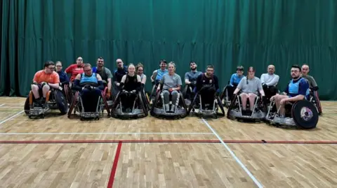 Stoke Mandeville Maulers  Stoke Mandeville Maulers players smiling for the camera during one of their recent training sessions. There is a green curtain behind them.