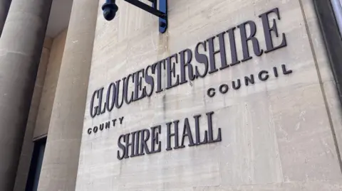 A photo showing the outside of Shire Hall in Gloucester. There's is a Gloucestershire County Council sigh on the side of a wall