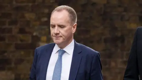Getty Images Richard Hughes, chairman of the Office for Budget Responsibility, wearing a white shirt, navy suit and light blue tie as he is pictured on Downing Street. 