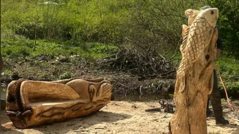The bench and post are sitting amid sawdust on the ground, finished without any paint on them.