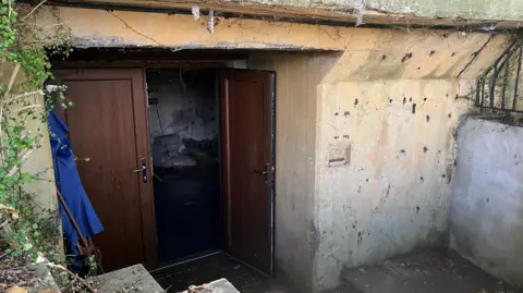 The image shows the exterior of a concrete building with brown wooden double doors.