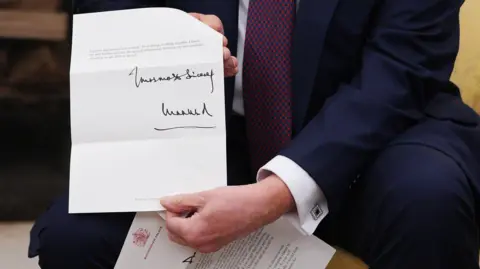 Getty Images Donald Trump shows a letter signed by the King inside the Oval Office after his meeting with Prime Minister Sir Keir Starmer