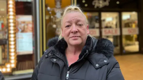 Donna Gosselin is looking at the camera. She has blonde hair and is wearing a black jacket. 