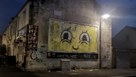 A billboard decorated with a large billboard, showing large eyes on a yellow face, similar to Spongebob Squarepants