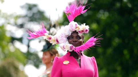 A black woman wears an ornate pink floral headress 