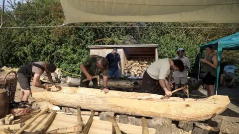 Rockingham Forest Trust Three men using hand tools while carving a log into a boat