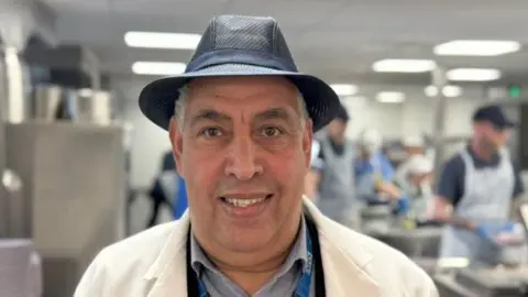 Qays Najm/BBC Ali Guenaoui, wearing a white catering overcoat and navy hat.