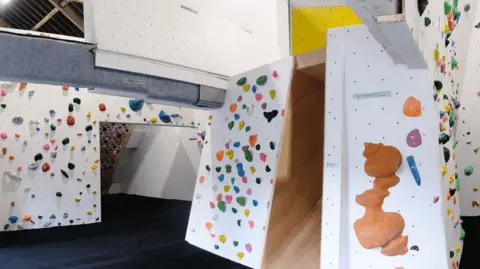 An indoor climbing wall. It has multicoloured footholds and a dark blue floor.