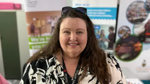 Fay Fleming-Horner has long dark hair and wears a black and white patterned dress with sunglasses perched on top of her head.