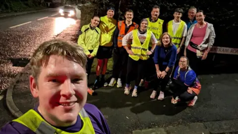 Scott Storey Scott Storey with fellow runners from the Hillsborough parkrun group, stood outside on a wet night in high-visibility jackets.
