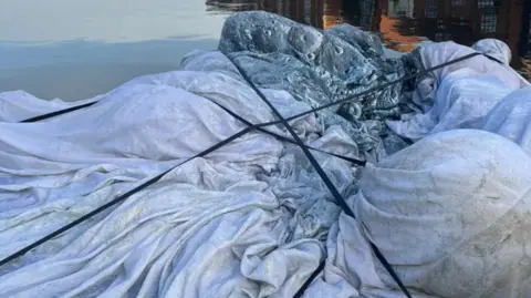 Bridgwater Town Hall The fabric of the moon, white and grey, deflated in the water. It is tied with black rope.