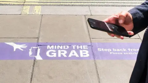 Getty Images Sign on the pavement says "mind the grab" and shows an image of a phone being snatched from a hand 