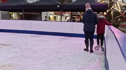 Ric Groves A parent and a child skating on a plastic ice rink