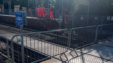 A blocked off tram line with workers milling in the background 