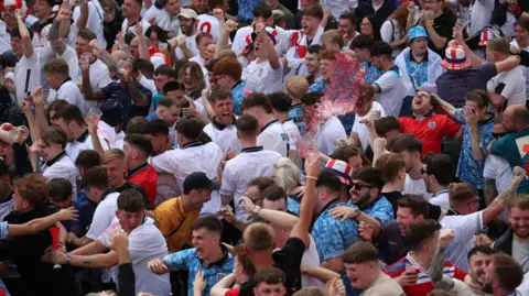 A crowd of men in football shirts jump and wave their arms in celebration at the theFans Central Park Fan Park in Newcastle watching the UEFA Euro 2024 Group C match between Denmark and England. 