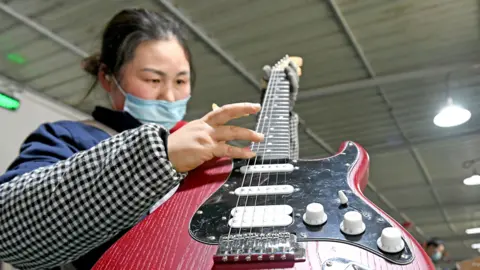 An woman holds a red electric guitar as she works on the production line of musical instruments for export at a workshop in Huainan, Anhui Province of China. 