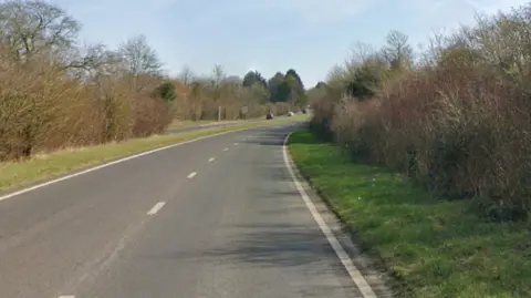 Google A two-lane road in the countryside daytime with cars in the distance