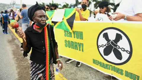 AFP via Getty Images People calling for slavery reparations, protest outside the entrance of the British High Commission during the visit of the Duke and Duchess of Cambridge in Kingston, Jamaica on 22 March 2022