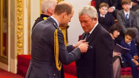 Prince William gives an MBE to a man in a black suit during an official ceremony 