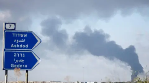 Reuters A blue finger signpost which points towards Ashdod and Gedera, where smoke is rising from the area.