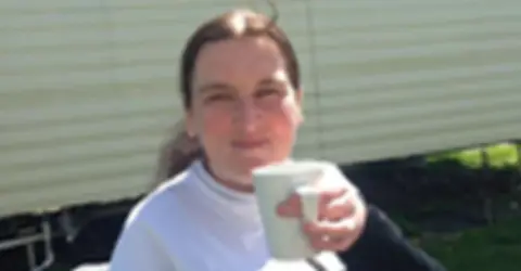 Police Scotland A woman smiling wearing a white t-shirt holding a mug outside of a caravan 