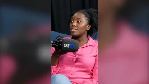 Psychologist Kimberley Wilson sits behind a BBC Radio 4 mic. She has black hair and wears a bright pink shirt
