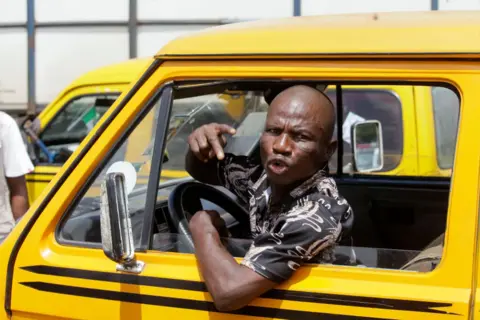 ADEKUNLE AJAYI / GETTY IMAGES A man shouts out the window of a yellow vehicle - Tuesday 1 October 2024