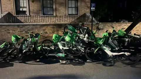 A huge pile of Lime bikes with bikes on top of each other in the street