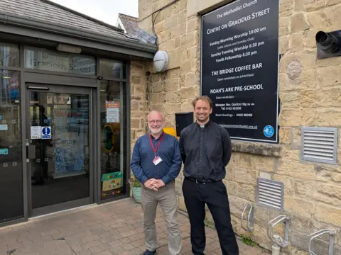 Tim O'Brien, Net Zero Officer for the Yorkshire North & East Methodist District - in a long-sleeved dark blue shirt and beige trousers - and the Reverend Gordon Hay - wearing a dog collar and dark trousers - standing outside Gracious Street Methodist Church in Knaresborough