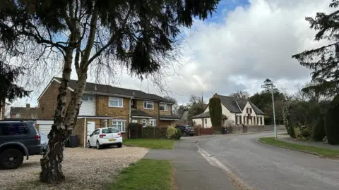 Kimberly Piper/BBC There is a tree on the left-hand side on a driveway with houses behind it. There is a road on the right-hand side of the photo.