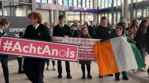 Pacemaker Press Protestors holding signs and an Irish tricolour at a demonstration calling for Irish language signs at Grand Central Station in Belfast. 